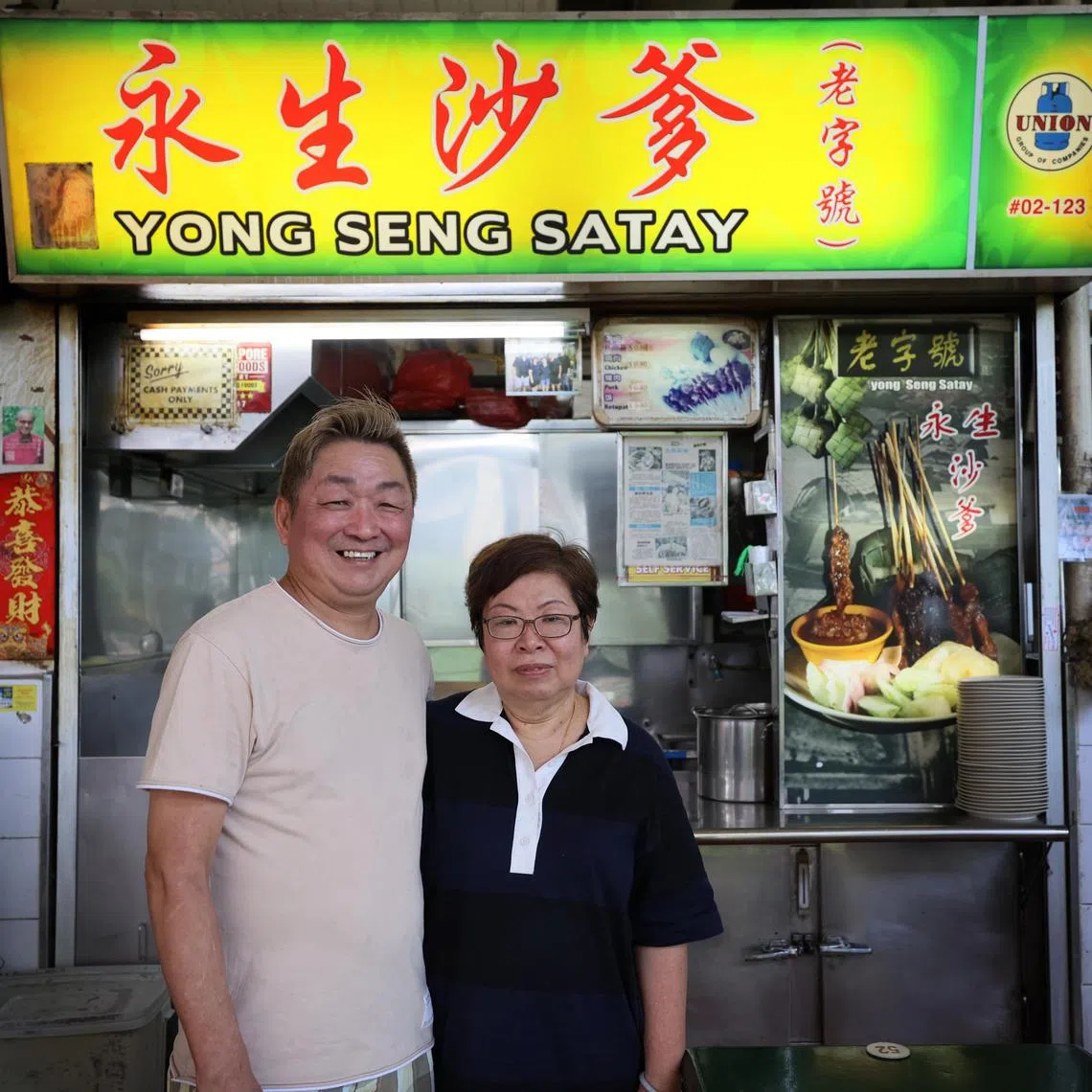张亚添（左）和太太符珍妮（右）属第三代小贩，一起经营沙爹生意。（龙国雄摄）