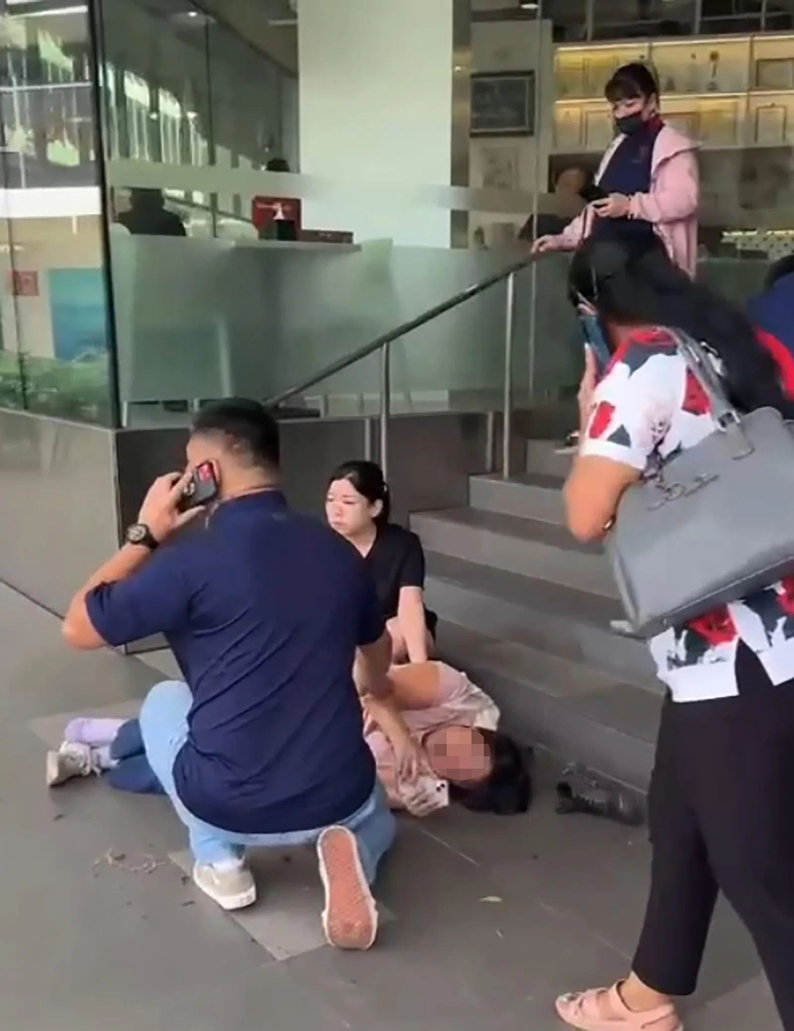 一名伤者坐在商场阶梯；另一名女伤者则侧躺在地上；最后一名伤者则坐在商场外的走道上，周围有超过10名公众协助。（受访者提供）