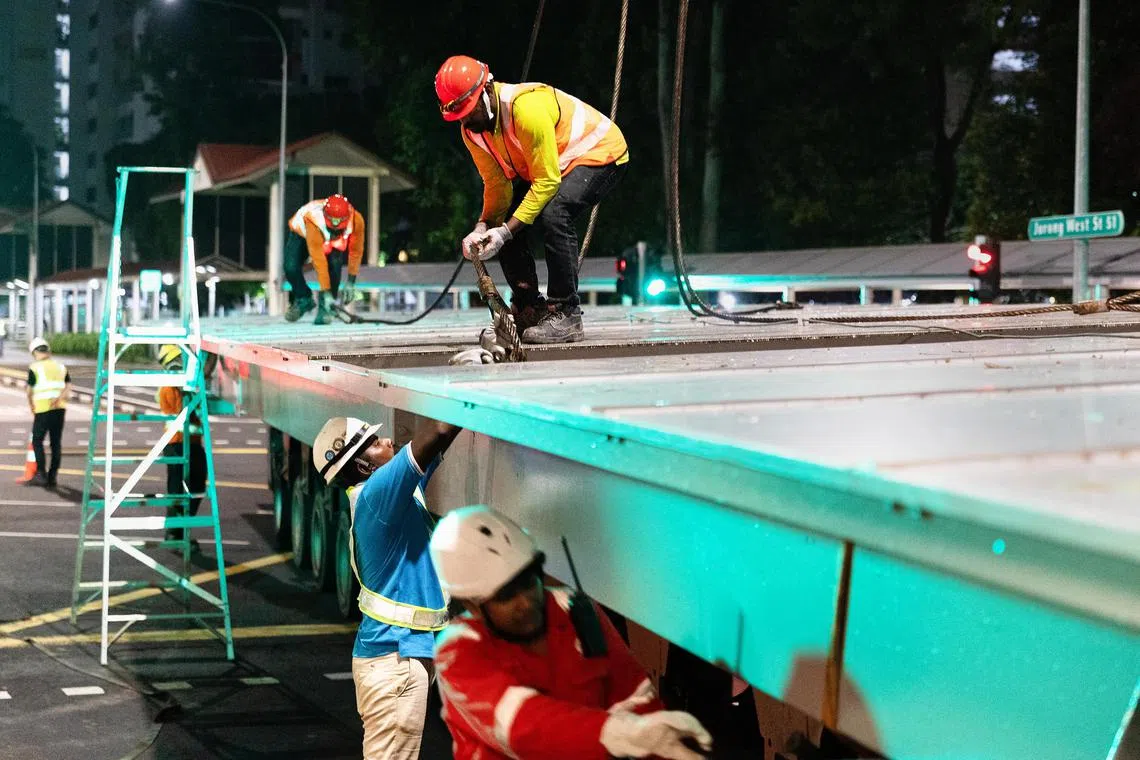 工人在起吊作业前，将起重机的钢索固定在屋顶结构的四个连接点上。（蔡家增摄）