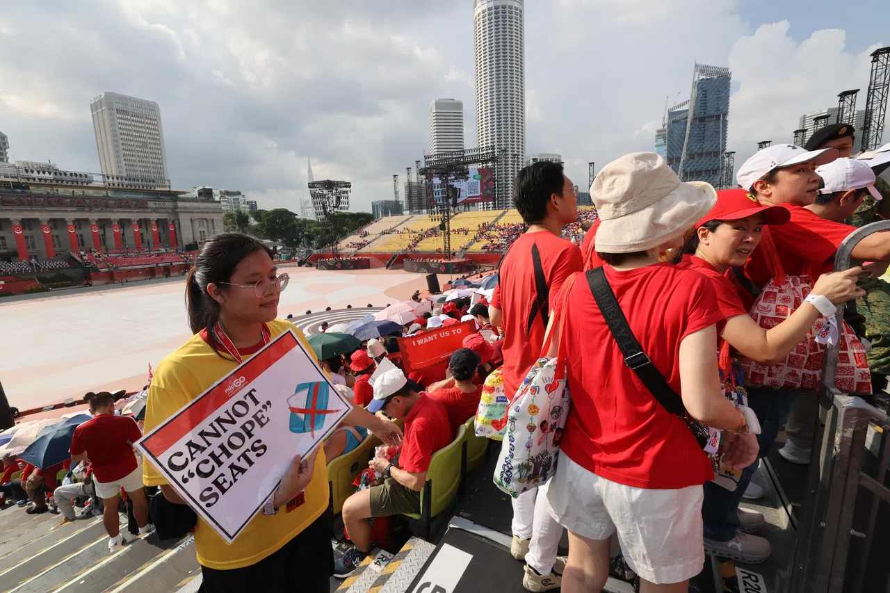 “不能占位”——政府大厦前大草场的好位置先到先得，不少观众在下午4时左右就已入场。工作人员举起牌子，提醒大家不要为他人占位。（邝启聪摄）