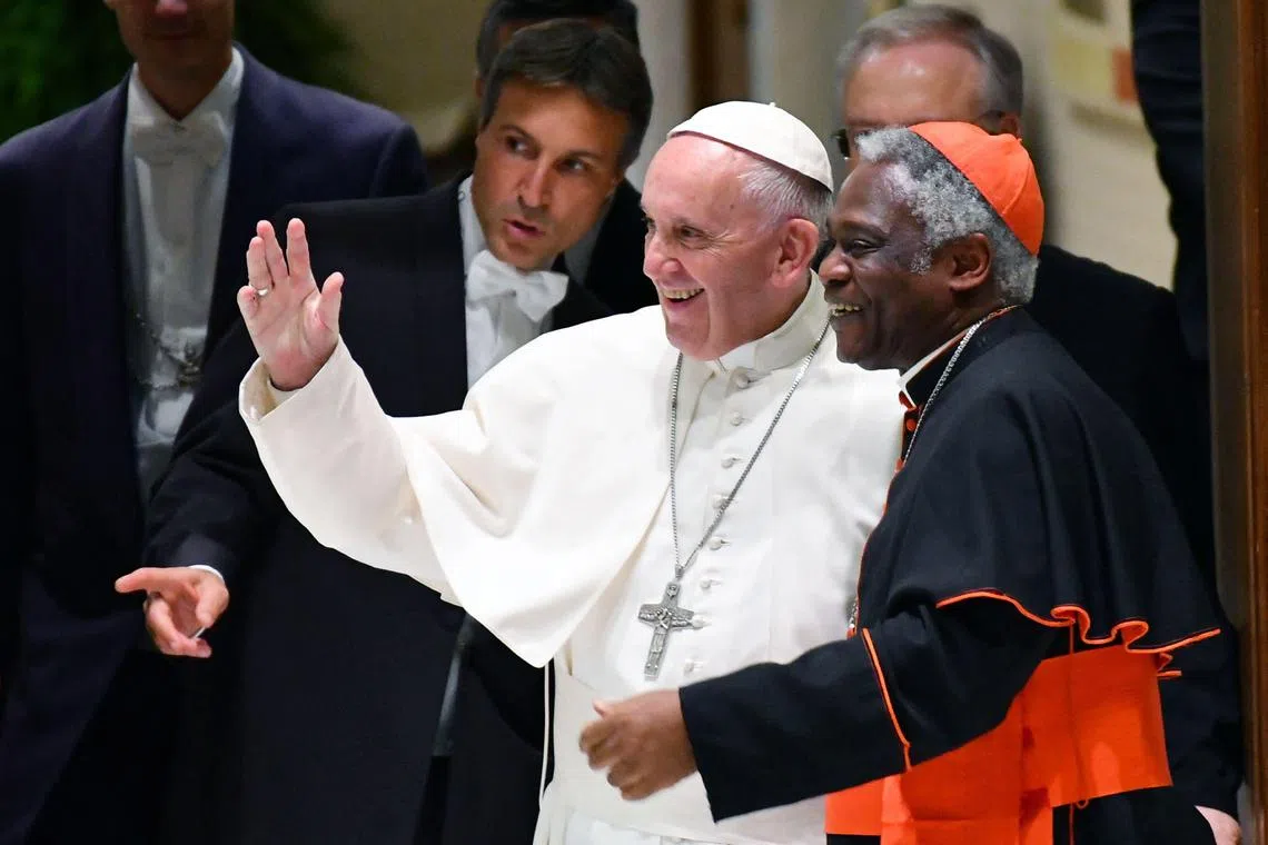 2011年11月5日，已故教宗方济各（中）和加纳籍枢机主教彼得·图克森（右）在梵蒂冈举行的一场活动上，向与会者致意。（法新社）