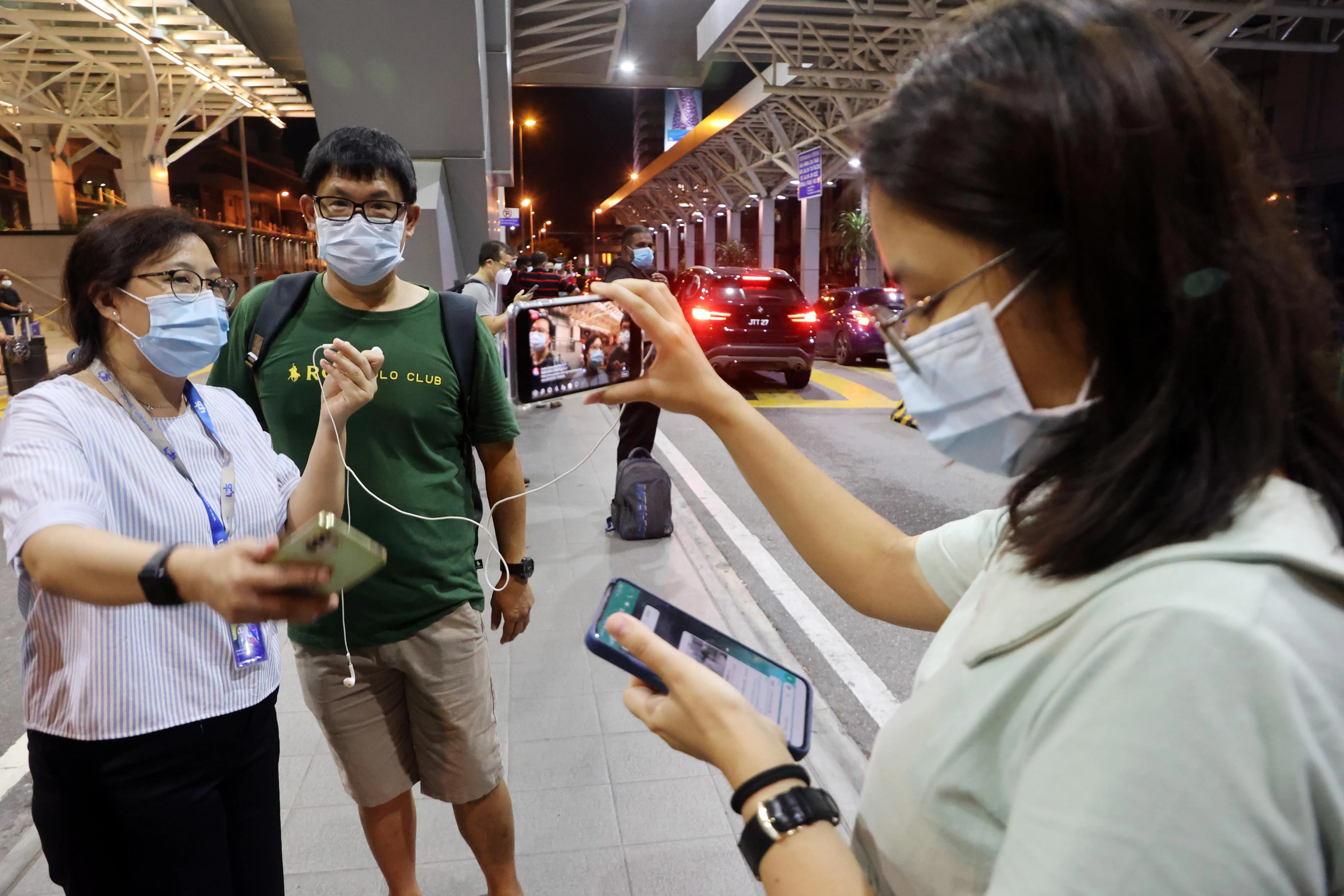 报道新马边境2022年4月1日全面重开的记者卢慧菁（左一）和姚可嘉（右一）在兀兰关卡进行《早现场》直播，现场访问凌晨通关回家的人。（邝启聪摄）