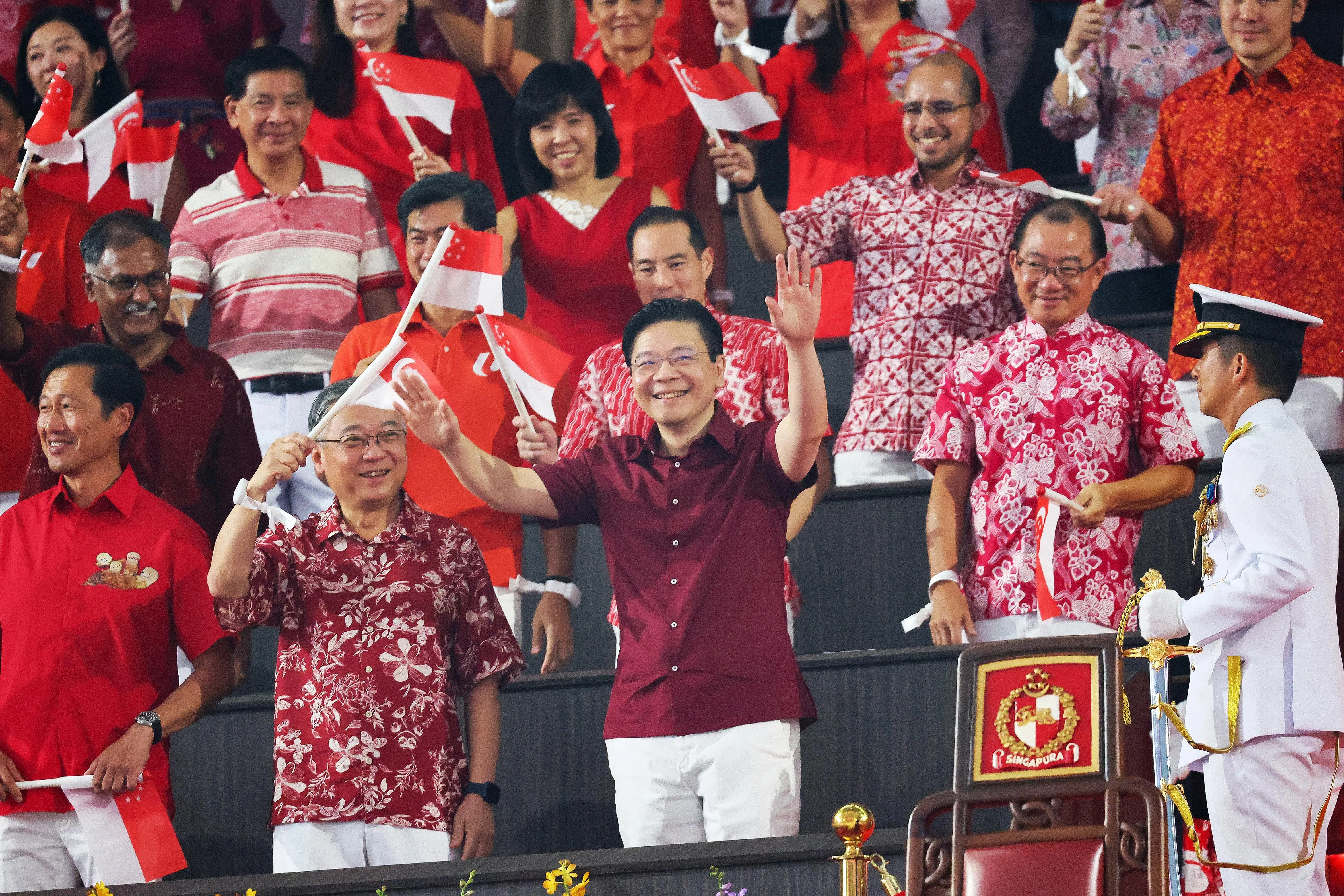 总理兼财政部长黄循财总理（前排左三）抵达国家体育场后，挥动双手回应热烈鼓掌的全场观众。他右手边依次是副总理兼贸工部长颜金勇和社会政策统筹部长兼保健卫生部长王乙康。第二排右起是国会议长谢健平、数码发展及新闻部兼保健卫生部高级政务部长陈杰豪、总理公署高级政务部长陈国明，以及律政部兼交通部高级政务部长穆仁理。（张俊杰摄）