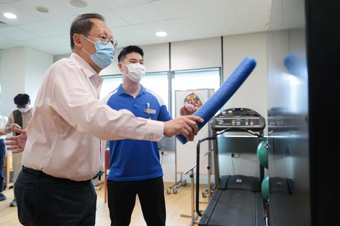 人力部长兼贸工部第二部长陈诗龙医生（左）星期四早上走访义顺社区医院复健治疗区时，在邱德拔医院物理治疗师洪伟显的指导下，尝试一般复建病人会进行的平衡运动。（李冠卫摄）