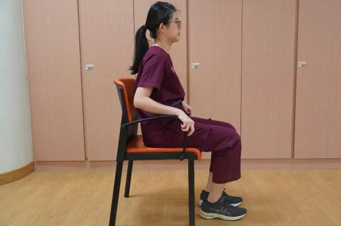 坐在有扶手的稳固椅子，但臀部稍微向前移。双手放在扶手上，双脚微张，脚板平放着地。（裕廊社区医院提供）