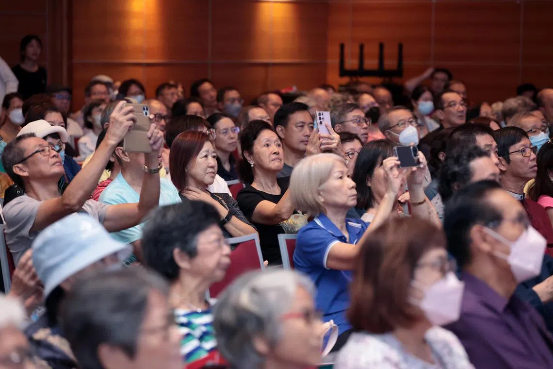 旅游分享会出席者举起相机拍摄投映在舞台布幕上的云南美照。（梁麒麟摄）