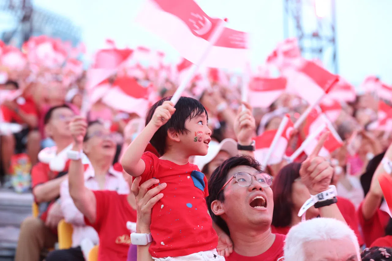 政府大厦前大草场化身红白海洋，从白发苍苍的老者到咿呀学语的孩童，人们穿上最靓丽的红白衣裳，自豪地挥舞手中的国旗，为新加坡60岁生日喝彩。（陈斌勤摄）