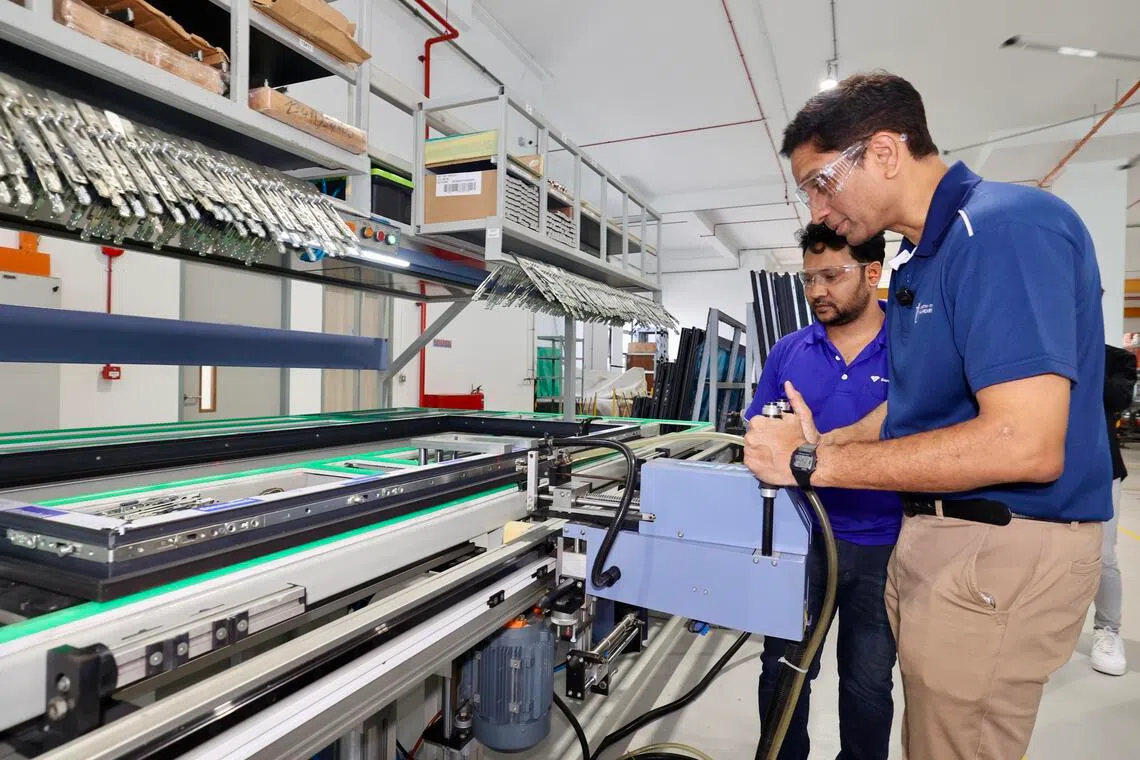 人力部兼文化、社区及青年部政务部长迪内希（右），在Sapphire Windows的生产车间，试用自动化设备安装窗户锁扣。（邬福梁摄）