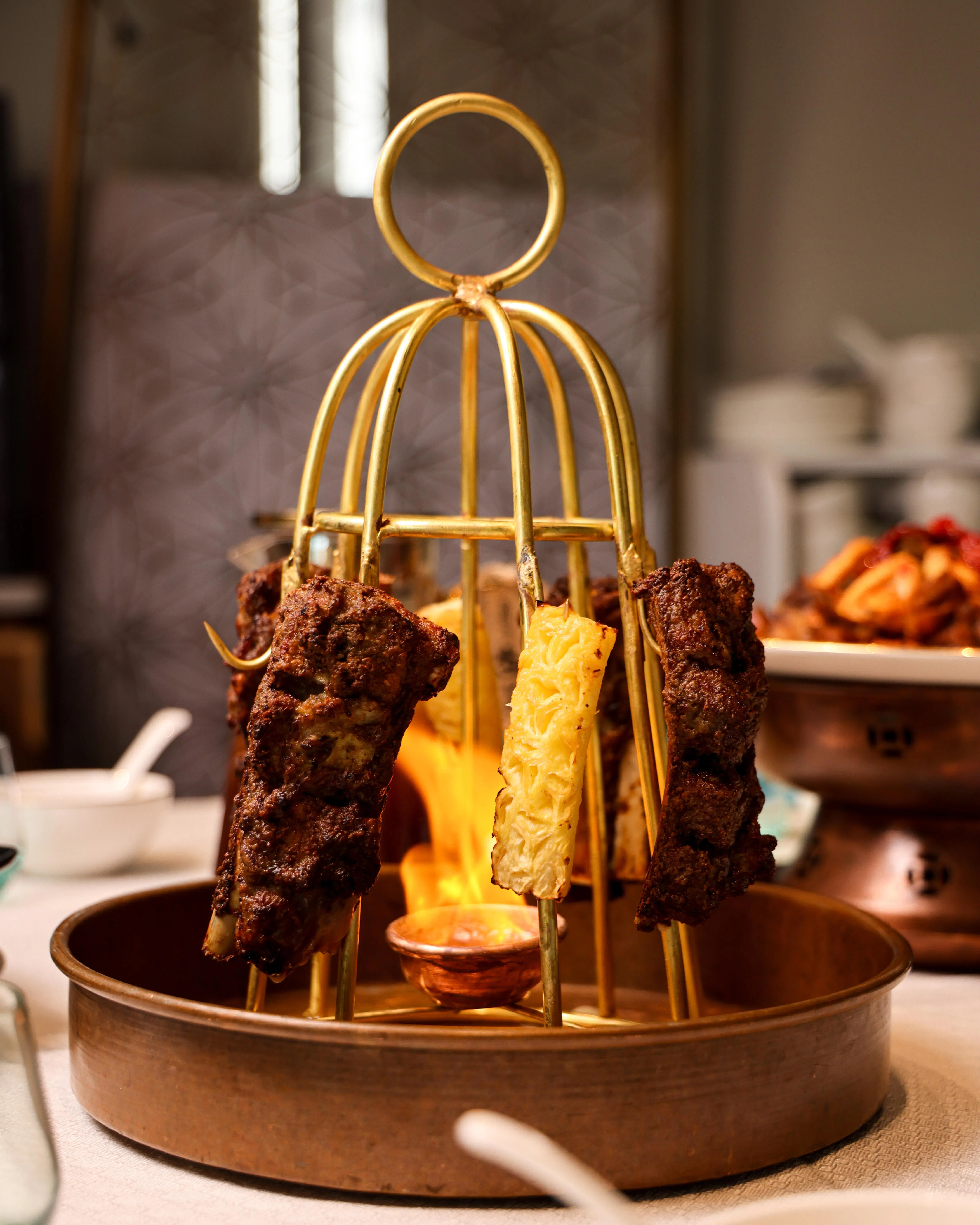 丝路馕坑架子肉伴随火焰上桌，羊肉炭烤得外皮微脆，内里多汁。（餐馆提供）