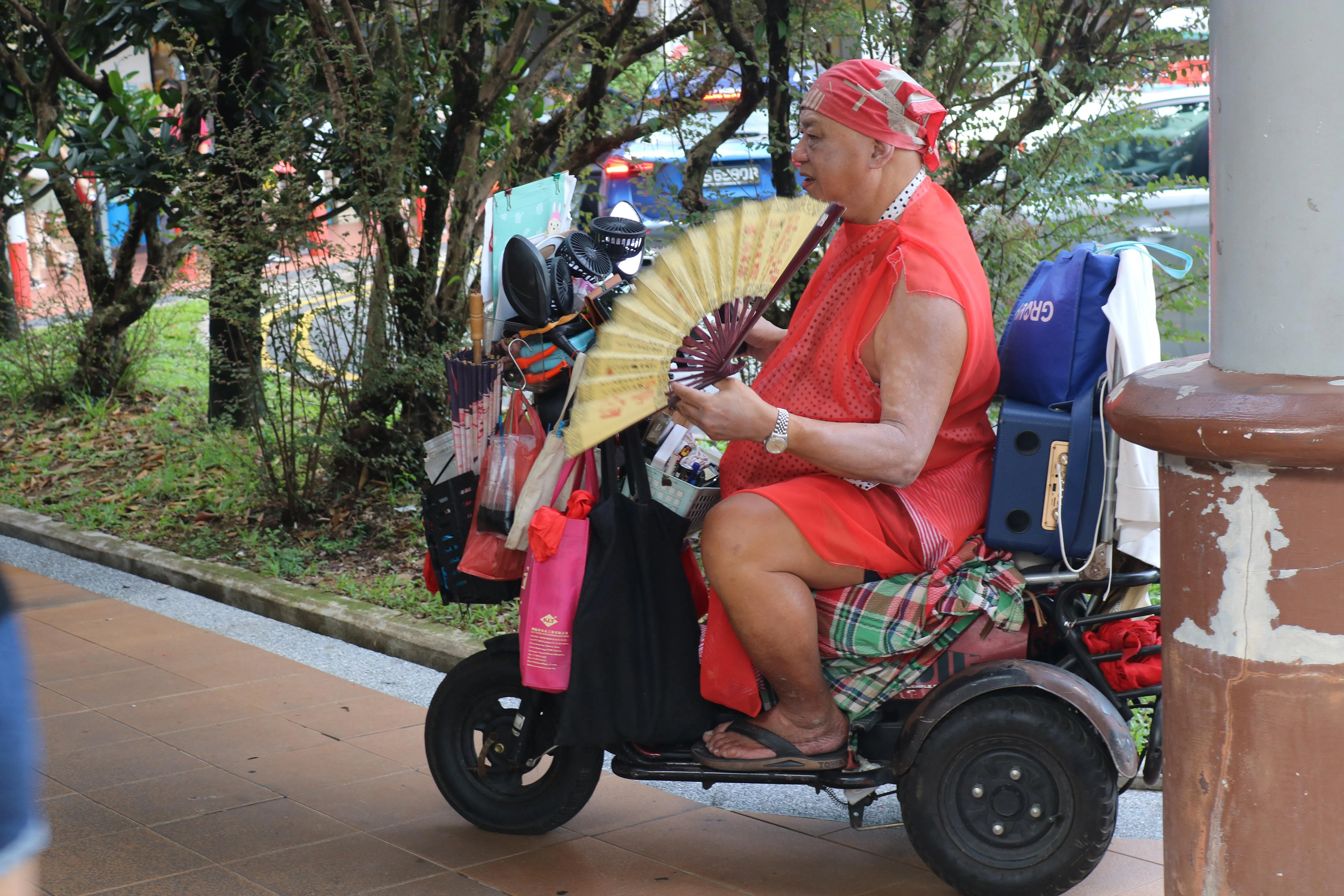 街头表演歌手罗任达在轮椅车上挂满丝带、纸伞等道具，配合歌曲旋律挥舞折扇。（刘文洁摄）