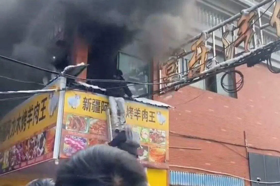浓浓黑烟把二楼店铺吞没，一名受困人员顺着梯子从阳台逃生。（路透社）