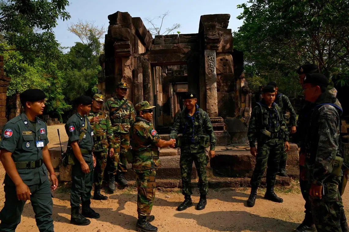 3月26日，一名柬埔寨士兵（中左）与一名泰国士兵（中右）在柬埔寨北部奥多棉吉省边境有争议的一所高棉古寺庙握手。（法新社）