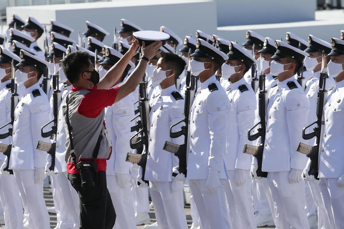 在今早的检阅礼上，一名海军人员的官帽不小心掉落，但由于不能随意移动身体，一名摄影师便帮他将帽子捡起和戴好。（蔡家增摄）