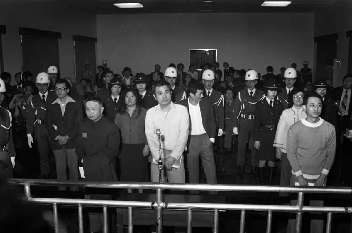 1980年3月，高雄美丽岛事件于警备总部军法处开庭，被告张俊宏（左一后戴眼镜者）、黄信介（左二手持外套者）、陈菊（左三裙装）、姚嘉文（中白衬衫）、施明德（右三蓄胡者）、吕秀莲（右二裙装）与林弘宣（右一）于法庭接受审判情景。（互联网）