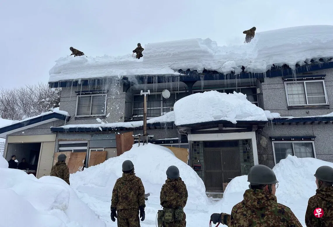 日本众院选战在严寒中举行，日本全国约42%的投票站包括北海道、青森等地预计在来临星期天投票日提早关闭。图为日本自卫队成员星期二在青森市协助居民清理屋顶上的积雪。 （法新社）