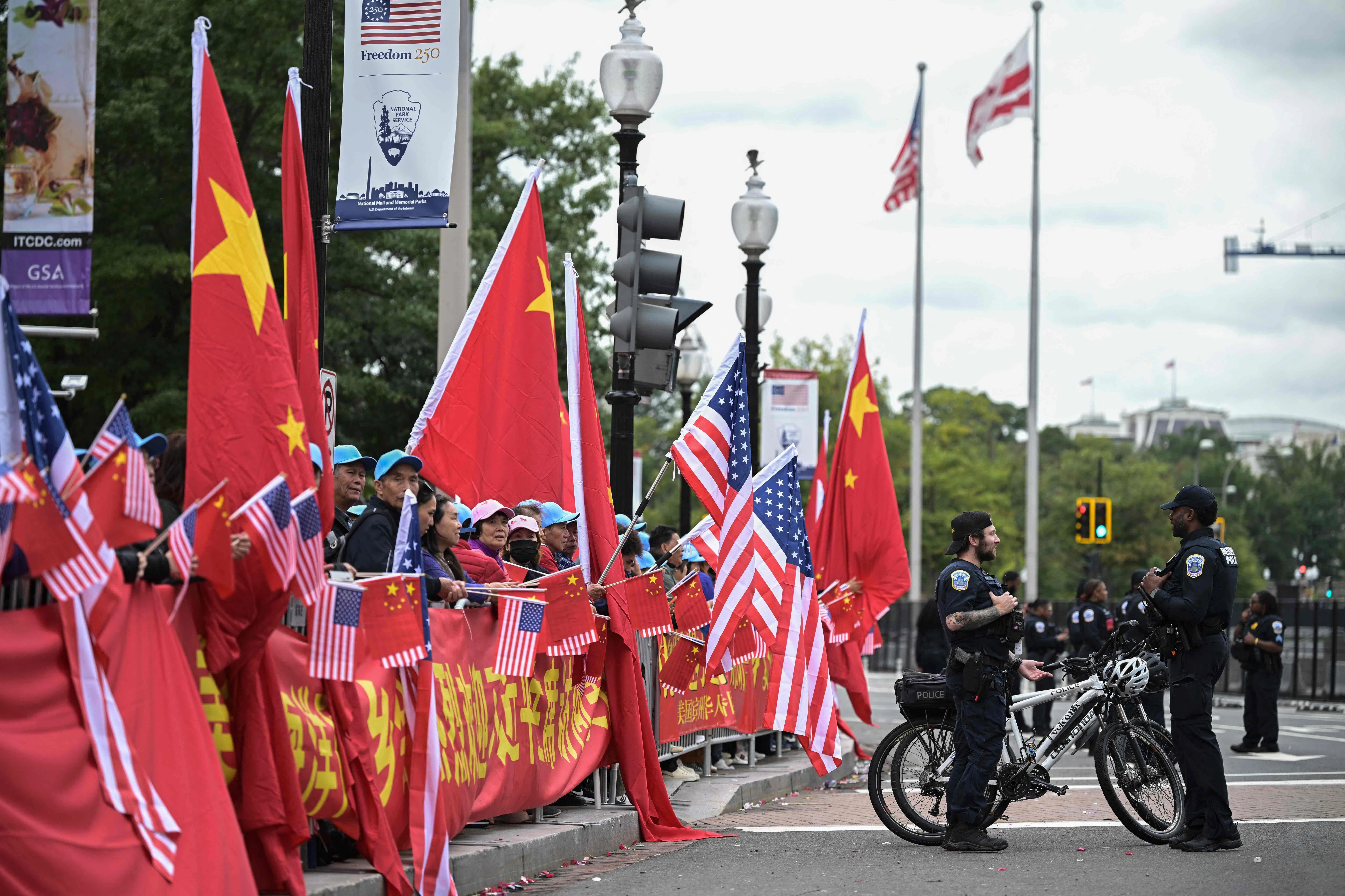 中国国家主席习近平访美之际，民众当地时间9月23日手持中美两国国旗，聚集在华盛顿华尔道夫酒店外，警员在旁执勤。为配合此次访问，酒店周边部分街道及人行道暂时封闭。（法新社）