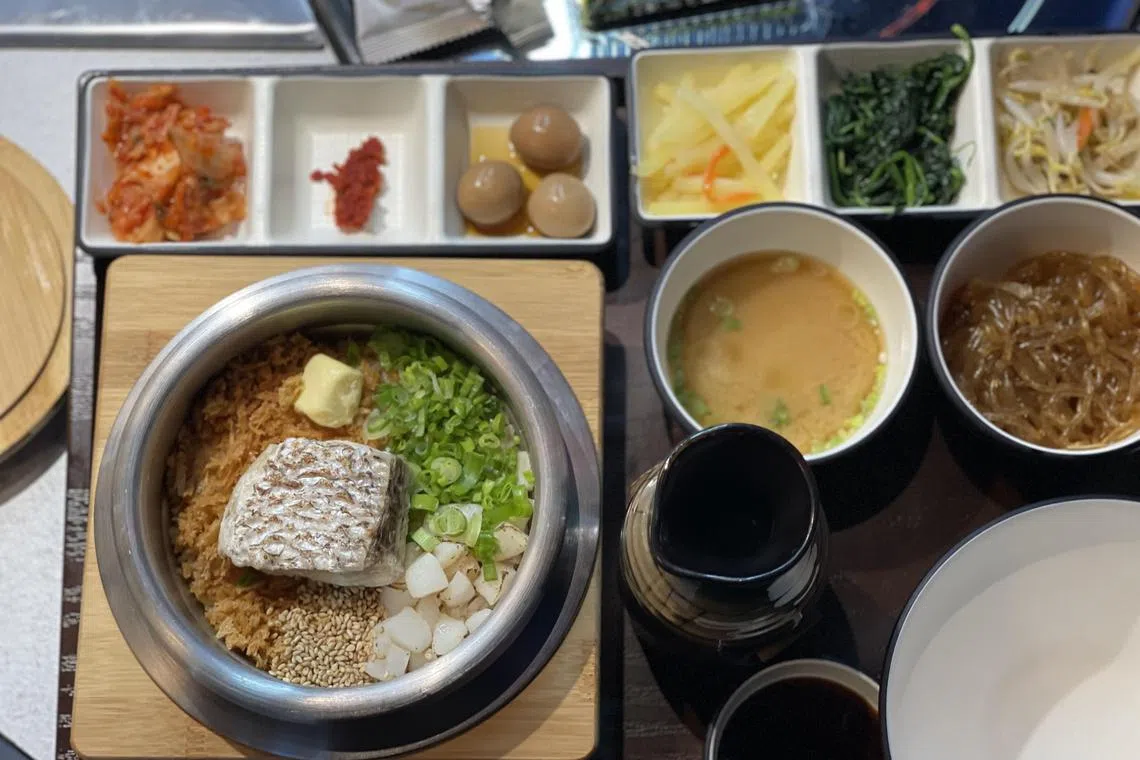 感炭鲷鱼石锅饭，鱼肉鲜甜软嫩，伴有多种小菜和酱料。（黄靖晶摄）