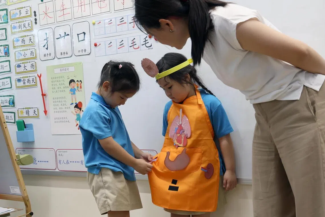 后港小学的MK@Hougang教育部幼儿园的幼二班（K2）孩童，日前上一堂延长30分钟的母语课堂时，经华文幼儿教师陈岑（右一）引导，将人体器官的图片卡贴在系围裙的同学身上，学习不同人体器官的华文名称、功能和位置。（梁麒麟摄）
