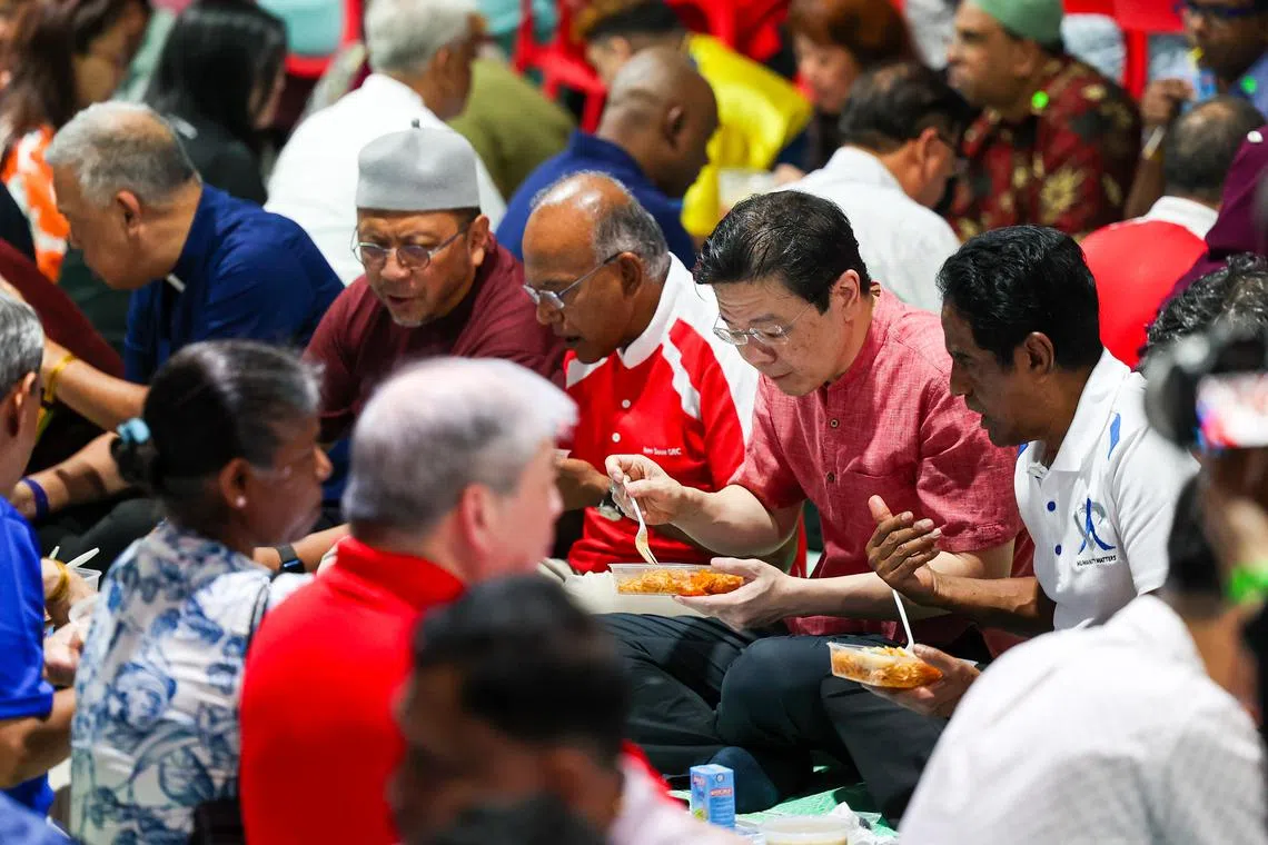 总理黄循财（右二）星期天（3月2日）在物资包装活动后，与义工、社区领袖和基层席地而坐，一起享用开斋饭食。出席者包括内政部长兼律政部长尚穆根（左三），以及新加坡仁心组织副主席马力肯（Noor Mohamed Marican，右一）。（林明顺）