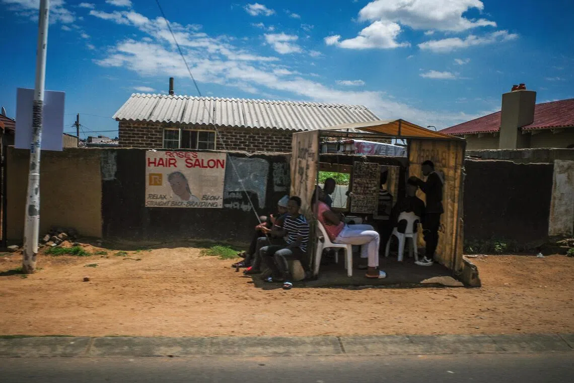 简陋的房子外，挂着理发广告布条，还有坐着等待理发的人。（叶振忠摄）