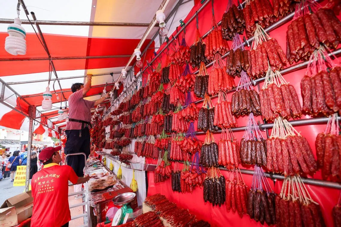 每年春节都在牛车水摆摊的广式腊味摊摊主叶伟强（站在楼梯者）星期六忙着挂腊味，准备在星期一正式开业。（陈斌勤摄）