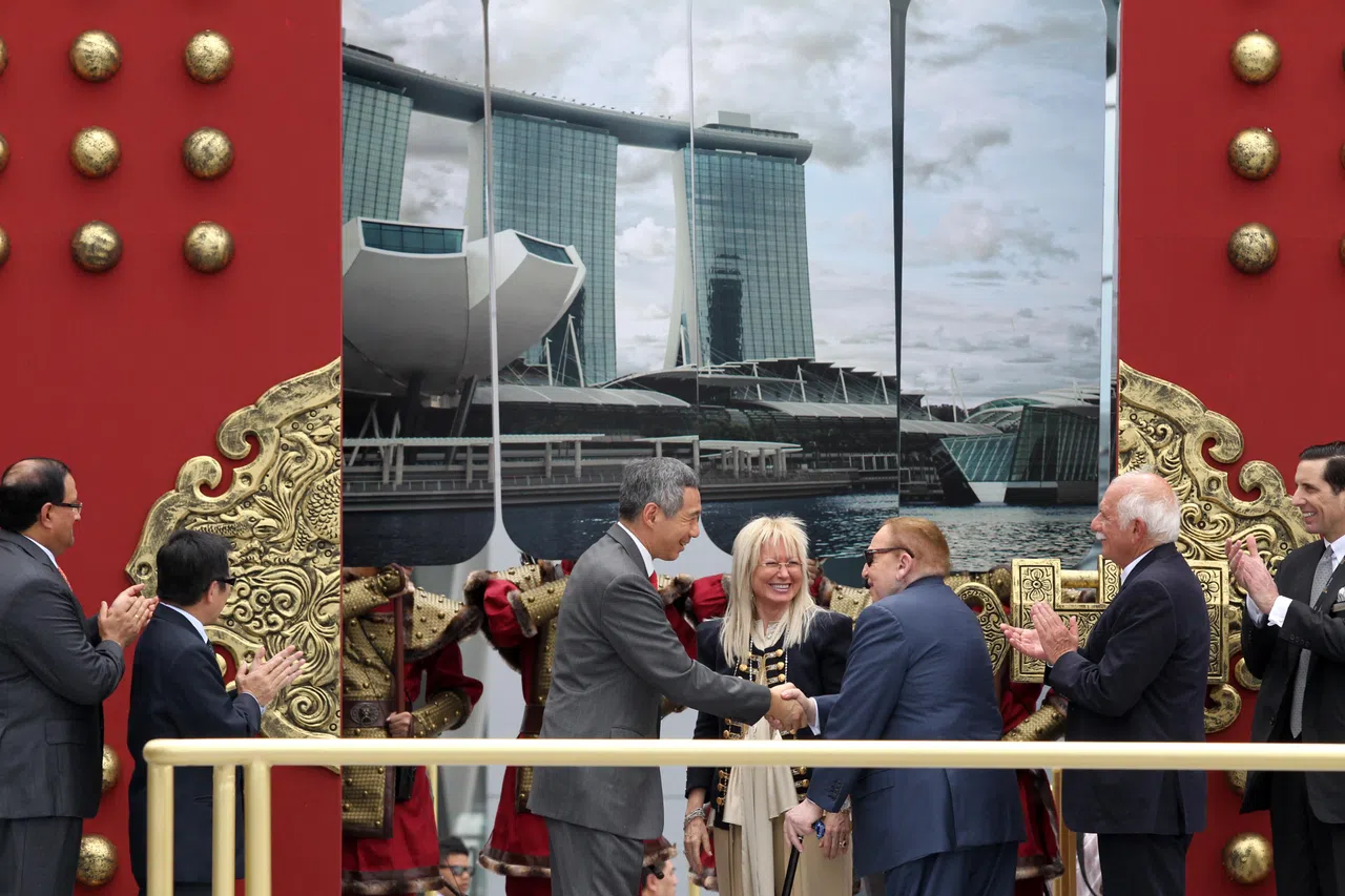 2011年2月17日，滨海湾金沙举行开幕仪式，朱门的大锁在吉时被打开，象征着门后外型近似巨型“莲花”盛开的艺术科学博物馆也正式开幕了。此时，拉斯维加斯金沙主席兼行政总裁艾德森（右三）满脸微笑地趋前同李显龙总理（左三）握手；台上的嘉宾包括时任国家发展部长马宝山（左二）和贸工部兼教育部高级政务部长易华仁（左一）。金沙的高级管理层代表和艾德森夫人米丽娅姆博士（右四）也鼓掌以示庆祝。（档案照片）