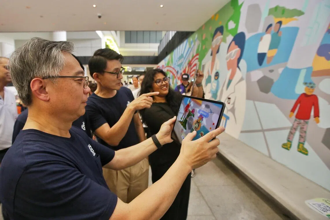 颜金勇（左一）在新工大学生指导下，利用数码平台peopleofpdd.sg创设虚拟角色，参与壁画在虚拟平台上的二次创作。马炎庆（左二）在一旁欣赏。（特约陈福洲摄）