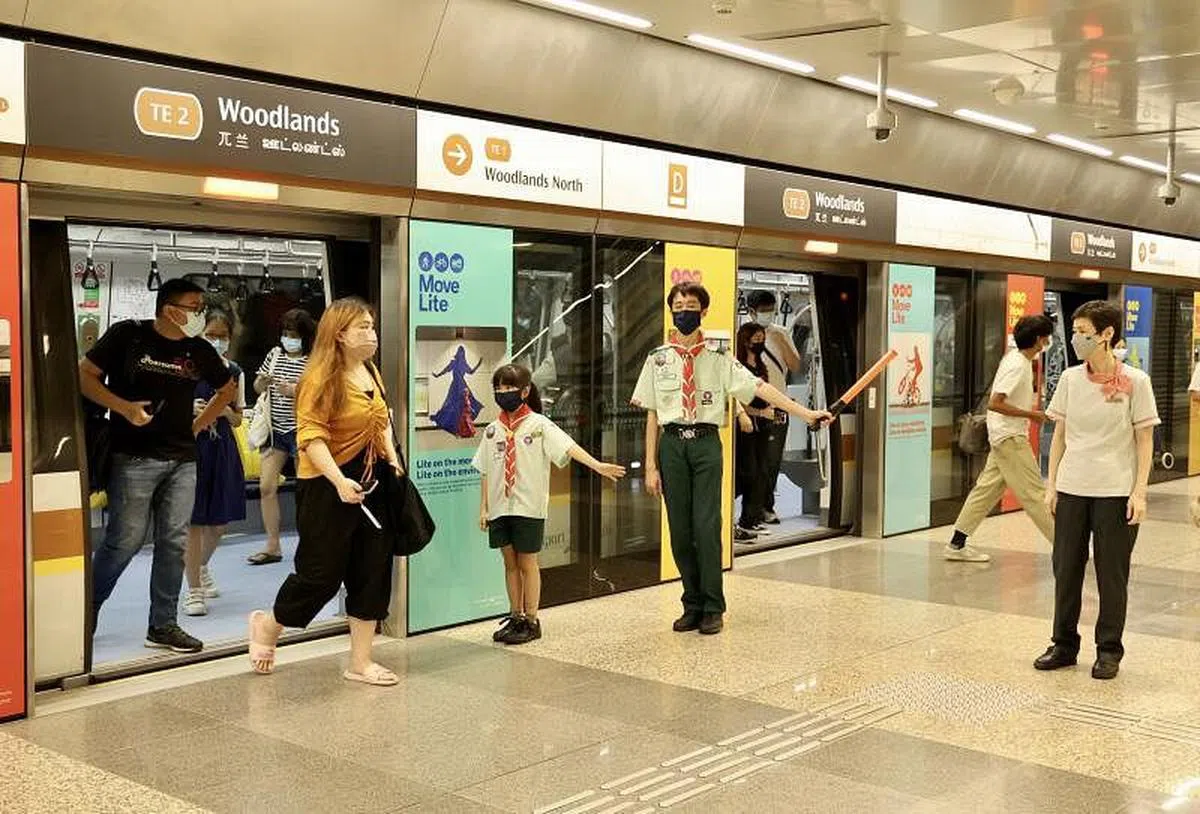 童军林思淇（左三）和罗庆轩在地铁月台，与SMRT服务大使余秀萍（右）一起指挥乘客人流。（邬福梁摄）