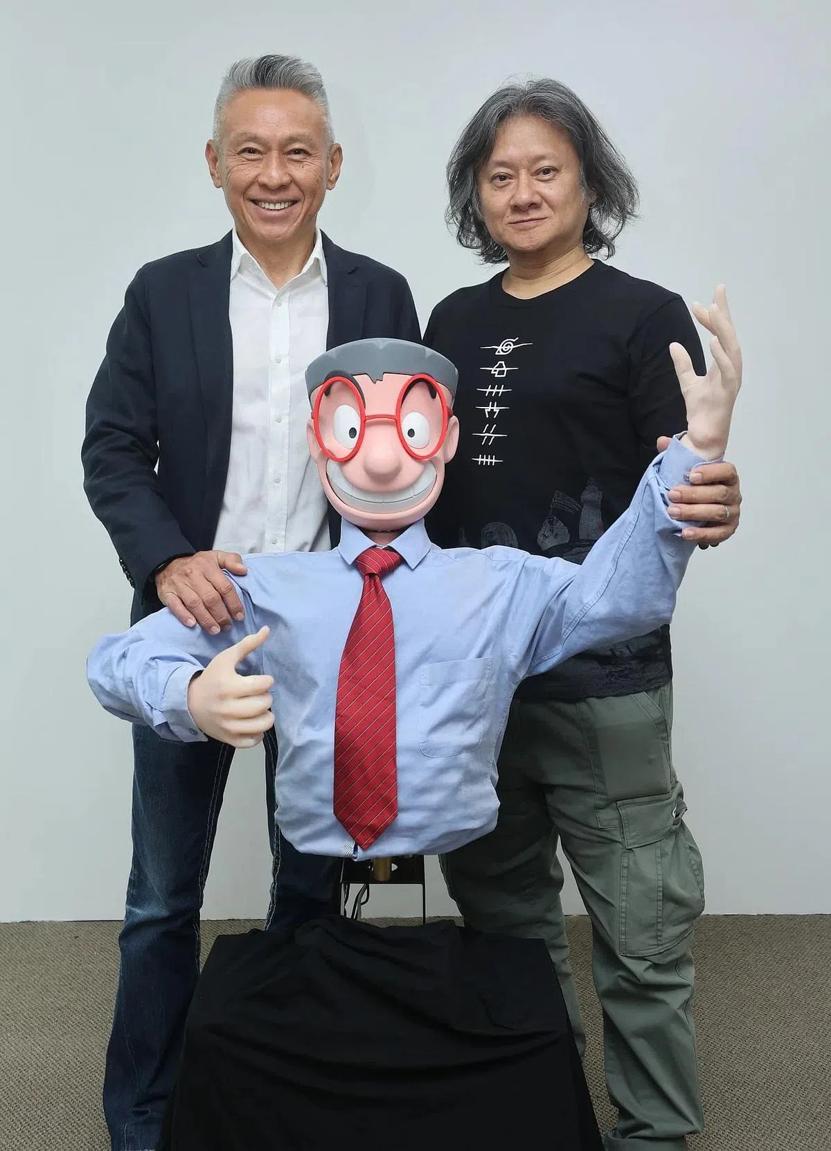 怕输先生如今也化身机器人，最大特色是能说Singlish。站在他身后的是Dex-Lab董事长卢源发（左）与怕输先生作者刘夏宗。（邬福良摄）